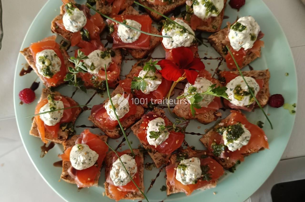 Assortiment de toasts au saumon fumé garnis de crème aux herbes, pesto et décorés de fleurs et framboises.