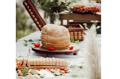 Pain rond et tranches de pain disposés sur une table décorée de feuilles et de pétales rouges en extérieur.