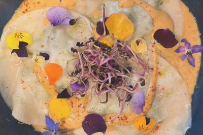 Assiette de ravioles garnies, décorées de fleurs comestibles colorées et de pousses, servies avec une sauce crémeuse.