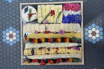 Plateau de fromages variés joliment disposés avec fleurs comestibles, fruits rouges et tomates cerises sur fond de carrelage.