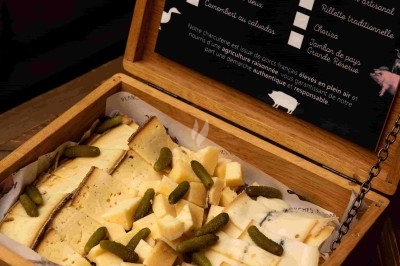 Coffret Assortiment de fromages coupés en morceaux, accompagné de cornichons, présenté dans une boîte en bois ouverte.