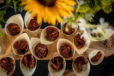 Cônes en bois remplis de tranches de saucisson disposés sur une table, avec un tournesol en premier plan flou.