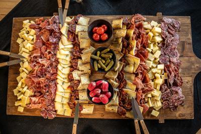 Plateau en bois garni de charcuteries, fromages, cornichons, tomates cerises et radis, avec des couteaux disposés.