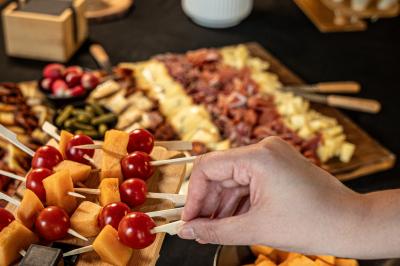 Main prenant une brochette de tomates cerises et melon sur un buffet composé de charcuterie, fromages et fruits.
