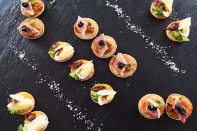 Assortiment de canapés variés disposés sur une ardoise noire, garnis de légumes, fromages et charcuteries.