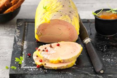 Bloc de foie gras tranché sur une planche avec couteau, accompagné de pain, confiture et grains de poivre.