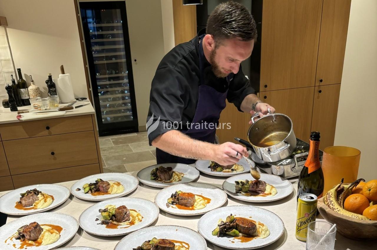 Un chef dresse des assiettes avec soin, ajoutant une sauce sur des plats à base de viande et légumes dans une cuisine.