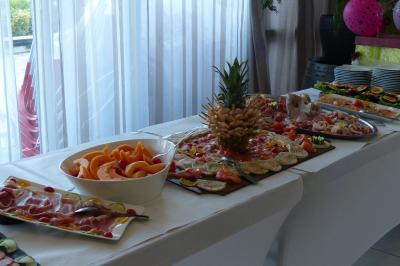 Buffet avec des plats variés comprenant fruits, charcuterie et légumes, disposés sur une table blanche près d'une fenêtre.