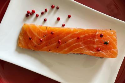 Tranche de saumon cru sur une assiette blanche, décorée de baies roses et d'herbes.