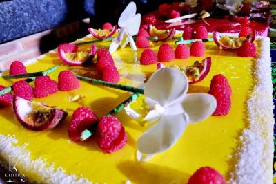 Gâteau décoré de framboises, fleurs en sucre et fruits de la passion sur un glaçage jaune vif.