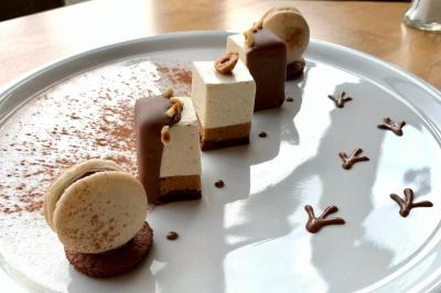 Dessert raffiné composé de mousses, macarons, chocolat et décorations en cacao sur une assiette blanche.