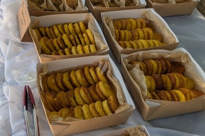 Buffet en plein air avec des boîtes contenant des biscuits, des pâtes et des beignets disposés sur une nappe blanche.