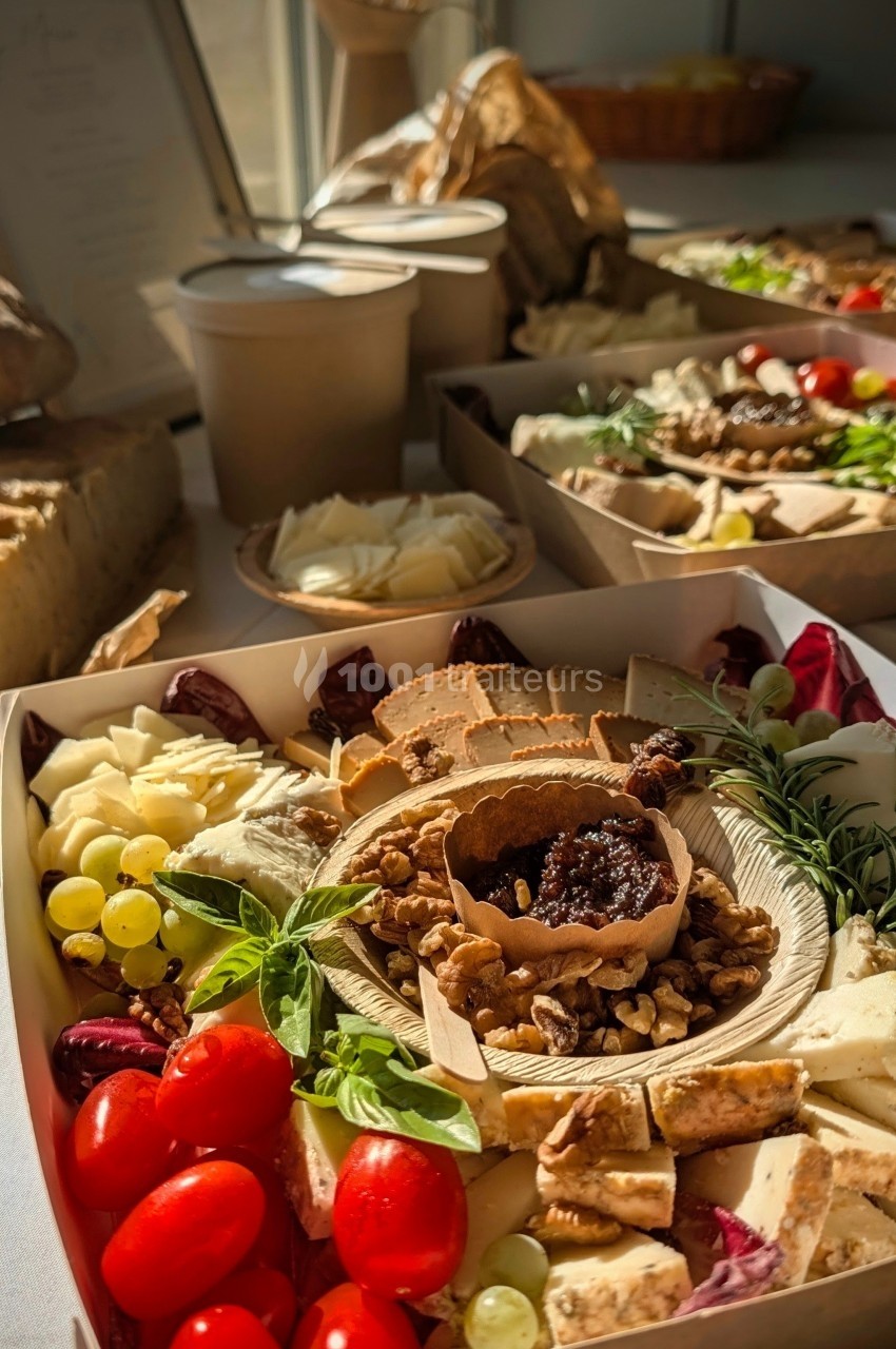 Plateau de charcuterie et fromages avec fruits, noix et légumes, présenté sur une table lumineuse.