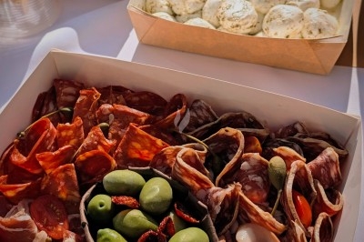 Plateau de charcuterie avec olives, tomates et viandes variées, accompagné de mozzarella et antipasti en arrière-plan.