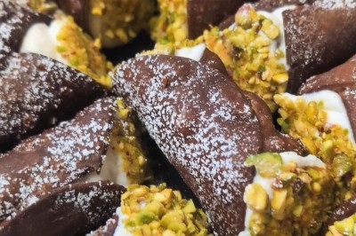 Cannoli au chocolat garnis de ricotta et décorés de pistaches concassées, saupoudrés de sucre glace.