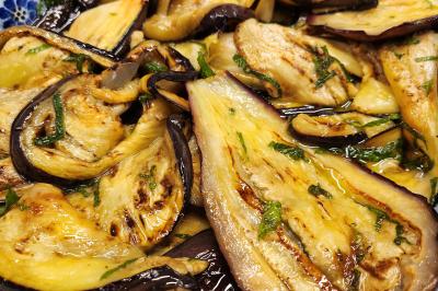 Tranches d'aubergines grillées assaisonnées d'huile, d'herbes fraîches et servies dans un plat à motifs bleus.