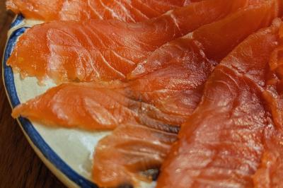 Tranches de saumon fumé disposées en éventail sur une assiette en céramique blanche et bleue, posée sur une table en bois.