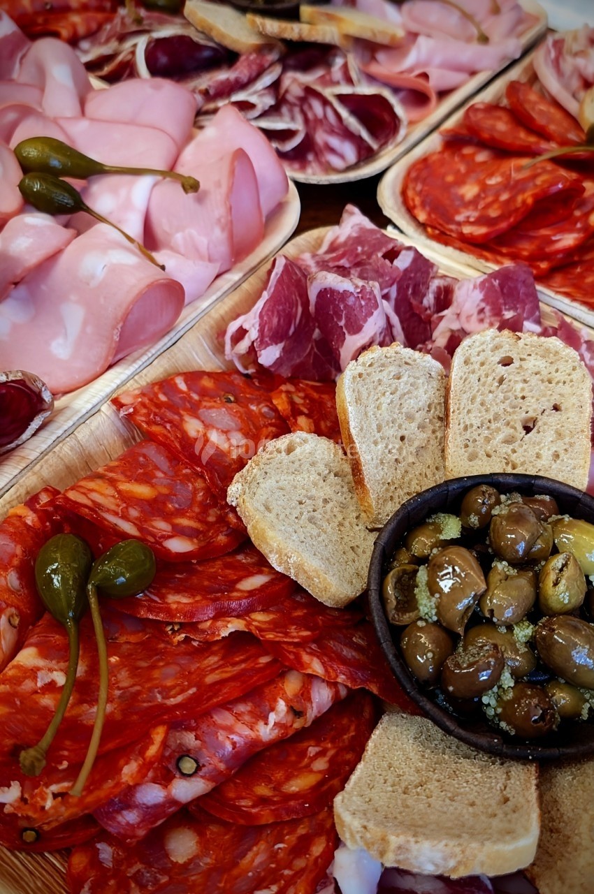 Plateau de charcuterie variée avec olives marinées, cornichons et tranches de pain disposés sur un plateau en bois.