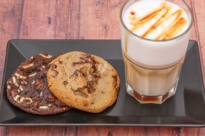 Assiette avec deux cookies aux pépites de chocolat et verre de latte macchiato sur une table en bois.