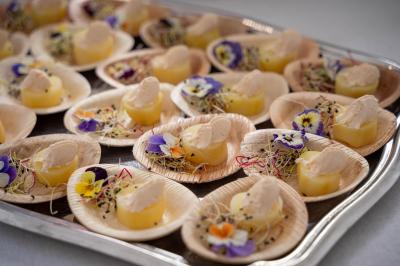 Assortiment de bouchées sur des assiettes en bois, décorées de fleurs comestibles et de pousses colorées.