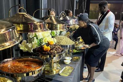 Buffet avec plats variés, une femme en tenue de service sert des invités dans un cadre élégant avec décoration florale.