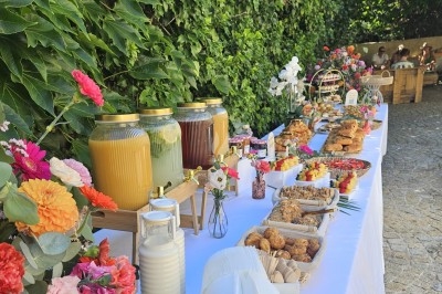 Buffet en extérieur avec boissons, viennoiseries, fruits et fleurs colorées sur une table blanche près d'un mur végétal.