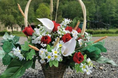 Traiteur Iles en Fete Magny-les-Hameaux #4 Panier en osier rempli de roses rouges, arums blancs, marguerites et feuillage, posé sur un sol gravillonné en extérieur.
