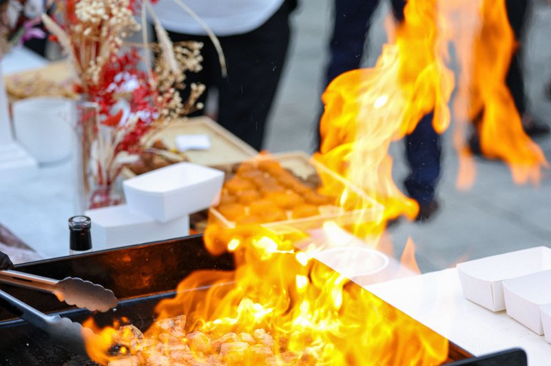 Viande grillée en cuisson sur une plancha avec des flammes vives, entourée de décorations florales et de convives en arrière…