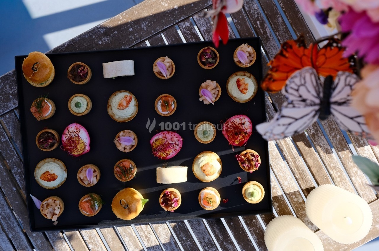 Buffets Cocktails Plateau de canapés variés disposés sur une table en bois, décorée de fleurs et de bougies.