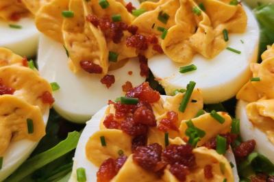 Œufs durs garnis de crème jaune, parsemés de morceaux de bacon croustillants et de ciboulette, sur un lit de salade.