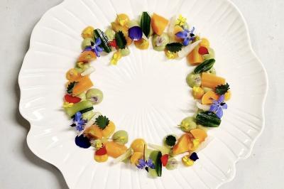 Assiette blanche décorée de légumes colorés, fleurs comestibles et herbes disposés en cercle.