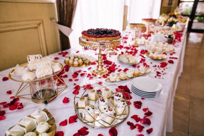 Table décorée avec des pétales de roses rouges, garnie de desserts variés et d'une tarte aux fruits sur un présentoir doré.