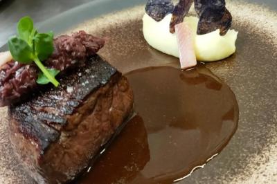 Plat gastronomique avec pièce de viande grillée, purée, chips violettes, sauce brune et garniture d'herbes fraîches.