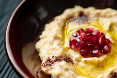 Traiteur La Beyrouthine Roquebrune-Cap-Martin #3 Purée de pois chiches garnie de graines de grenade, huile d'olive et épices, servie dans un bol brun.