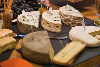 Assortiment de fromages variés présentés sur une table, avec étiquettes et raisins en arrière-plan.