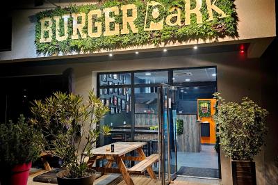 Façade d'un restaurant avec enseigne lumineuse ’Burger Park’, terrasse en bois et plantes décoratives.