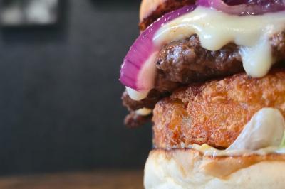 Burger avec steak, fromage fondu, rondelles d'oignon rouge et galette croustillante, posé sur une table en bois.