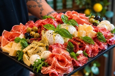 Traiteur Pasta Da Nonna Mia Bouc-Bel-Air #4 Plateau de charcuteries et fromages avec burrata, olives, tomates séchées, artichauts et basilic, tenu par une personne.