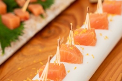 Dés de saumon frais sur des pics en bois, présentés sur un support blanc avec des zestes d'agrumes.