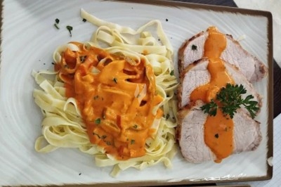 Assiette avec des tagliatelles nappées de sauce tomate crémeuse et des tranches de rôti garnies de persil.