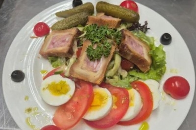 Assiette composée de pâté en croûte, œufs durs, tomates, cornichons, olives et salade verte, garnie de persil.