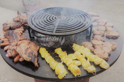 Viande et brochettes de poulet grillant sur un barbecue circulaire avec grille au centre.