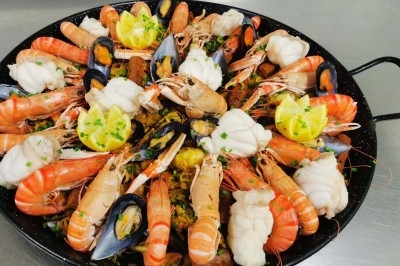 Plat de paella garni de fruits de mer variés, dont crevettes, moules et morceaux de poisson, décoré de quartiers de citron.