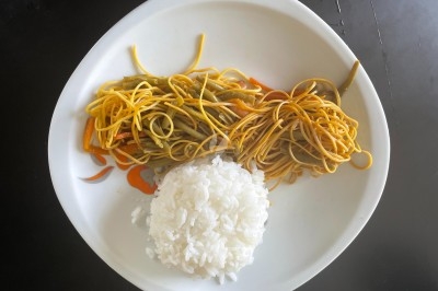 Chao Men Assiette contenant des nouilles sautées aux légumes et une portion de riz blanc, posée sur une table noire.