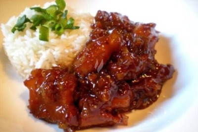 Porc caramel Plat de poulet caramélisé accompagné de riz blanc garni de ciboulette sur une assiette blanche.