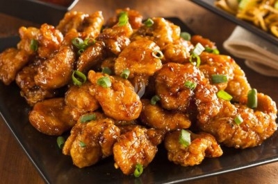 Poulet frit sauce citron Morceaux de poulet frit nappés de sauce brillante, garnis de ciboulette, servis sur une assiette noire.