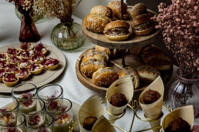 Plateau de mini-burgers, verrines, bouchées et fleurs séchées disposés sur une table pour un buffet.