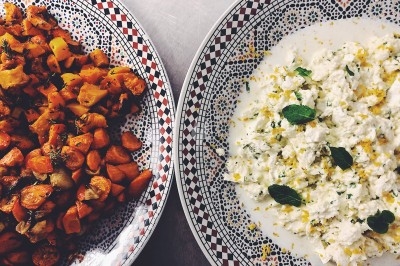 Traiteur La Tricoterie Traiteur Saint-Gilles #2 Assiette de légumes rôtis à gauche et plat de salade crémeuse garnie de menthe à droite, sur une table.