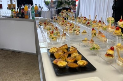 Buffet de cocktails avec une variété de bouchées et boissons disposées sur une table blanche dans un espace lumineux.