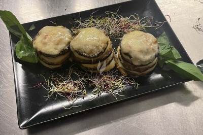 Assiette contenant trois millefeuilles d'aubergines gratinées, décorée de pousses et de feuilles vertes.